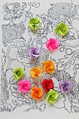 Röschen aus Papier auf einer Folie mit aufgemaltem Blumenmuster