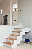 Staircase with glass balustrade in interior with traditional fireplace