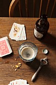 Guinness in Flasche und Glas, Flaschenöffner, Erdnüsse und Spielkarten auf Holztisch