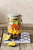 South Western Style bean salad lunch jar on a ceramic tile with lime wedges and stone back ground