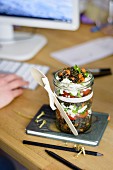 Lentil salad with carrots, tomatoes and feta in a glass jar, at an office