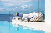 White outdoor furniture next to pool with view of sea and clouds in blue sky