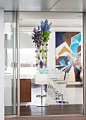 Vertical flower arrangement on tall table next to modern bar stools