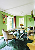 Massivholz-Tisch, Vintage Bänke mit Rentierfellen und Sessel mit Samtbezug in grünem Esszimmer mit Büffelschädel an der Wand