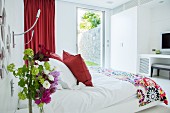 Red accents and floral patterns in white bedroom