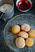 Donuts in a wire basket, a cup of jam and a can of icing sugar