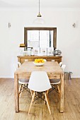 Rustic wooden table with white shell chairs, console table and rammed wall mirror in the background