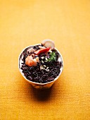 Black rice risotto with shrimps in a small bowl on a yellow background