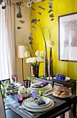 Festively set dining table in front of flower arrangement and yellow wall