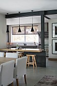 View past dining table into open-plan kitchen with breakfast bar and bar stools