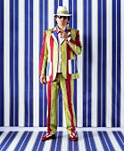 Man wearing brightly striped suit and hat against blue and white striped wall