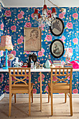 Ornaments on table and two chairs in front of pictures on floral wallpaper