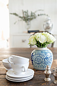 Stack of white teacups and saucers and Oriental vase of white roses on wooden table