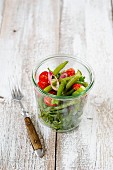 A bean and rocket salad with cocktail tomatoes and onions in a glass with a fork