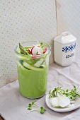 Pea and asparagus cream soup with radish slices in a glass jar