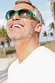 A man with grey hair wearing a white T-shirt and green sunglasses