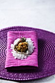 A breaded oyster on a bed of salt served on purple napkin and placemat