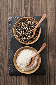 Black and white pepper and coarse sea salt with spoons in small bowls