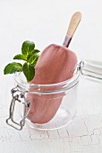 Raspberry ice cream on a stick with mint in a glass jar