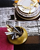 Crockery and gold cutlery on newspaper