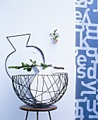 Vase and branch of unripe figs in delicate wire basket