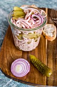 Sausage salad with red onion and gherkins in a glass on a wooden board