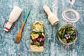 Quinoa and orzo pasta salads in glass jars, with dressing and a wooden fork