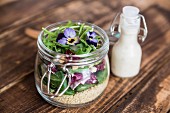 A quinoa salad with lambs lettuce, radicchio, rocket, croutons, goat's cheese and horned violets in a glass jar, with dressing in a glass bottle