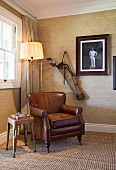 Brown leather armchair and standard lamp below vintage photo and golf bag in corner