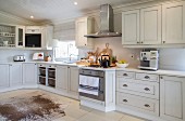 Gas cooker, stainless steel extractor hood and animal-skin rug on tiled floor in white country-house-style kitchen