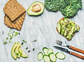 Sandwich with avocado, cucumber, kale, kress sprouts, pumpkin seeds over marble background
