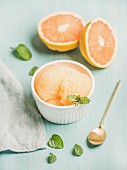 Pink grapefruit sorbet with fresh mint in white bowl over blue painted background