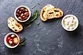 Olives, stuffed Peppers, mini Mozzarella cheese and sliced Ciabatta bread on dark background