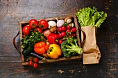 Frisches Gemüse in Holzkiste und Salat in Papiertüte auf Holzuntergrund (Aufsicht)