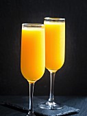 Zwei Gläser mit frisch gepresstem Orangensaft vor schwarzem Hintergrund