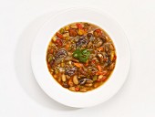 A bowl of bean soup in front of a white background (seen from above)