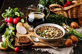 Cold Soup Okroshka with sausage, vegetables and kvass serving size in bowl and raw ingredients on wooden table