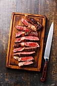 Sliced medium rare grilled beef Ribeye steak on cutting board and kitchen knife on wooden background