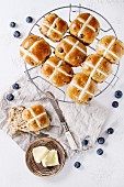 Hot cross buns on baking rack served with butter, fresh blueberries, knife and jug of cream