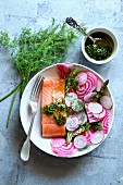 Spring salad with radish, chioggia beet, asparagus with a piece of smoked salmon and dill dressing on a plate