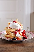 A stack of waffles with cream and fresh berries on a plate