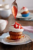 Strawberry sauce dripping from a spoon onto a cupcake with white frosting