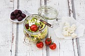 Zoodles (zucchini noodles) in a glass jar with tomatoes, feta and olives