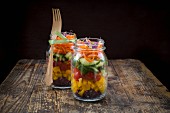 Rainbow salad in glass jars with red cabbage, yellow pepper, tomato, cucumber, carrots and beetroot sprouts