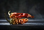 Two dried red chilli peppers in front of a dark background