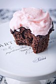 A Single Chocolate Cupcake with Pink buttercream Frosting with Bite Taken Out on Cakestand