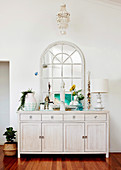 White chest of drawers with decorative objects and arched mirror