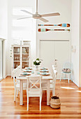 Laid dining table with white wooden chairs under ceiling fan