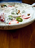 Vanilla yogurt with sliced strawberries and kiwi berries (mini kiwi), on a speckled plate on a wooden tray