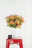 Flowers in glass vase covered in paper with graphic pattern arranged on red stool